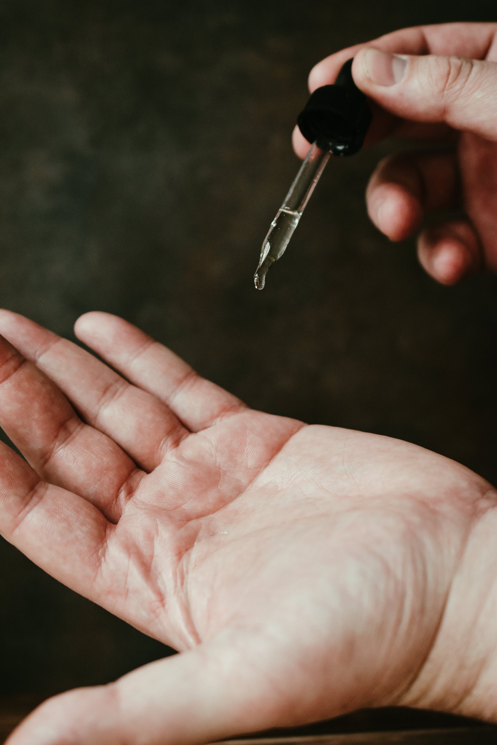 Hand holding a beard oil dropper with a dark background